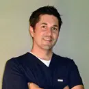 A man in navy blue scrubs smiling with arms crossed.